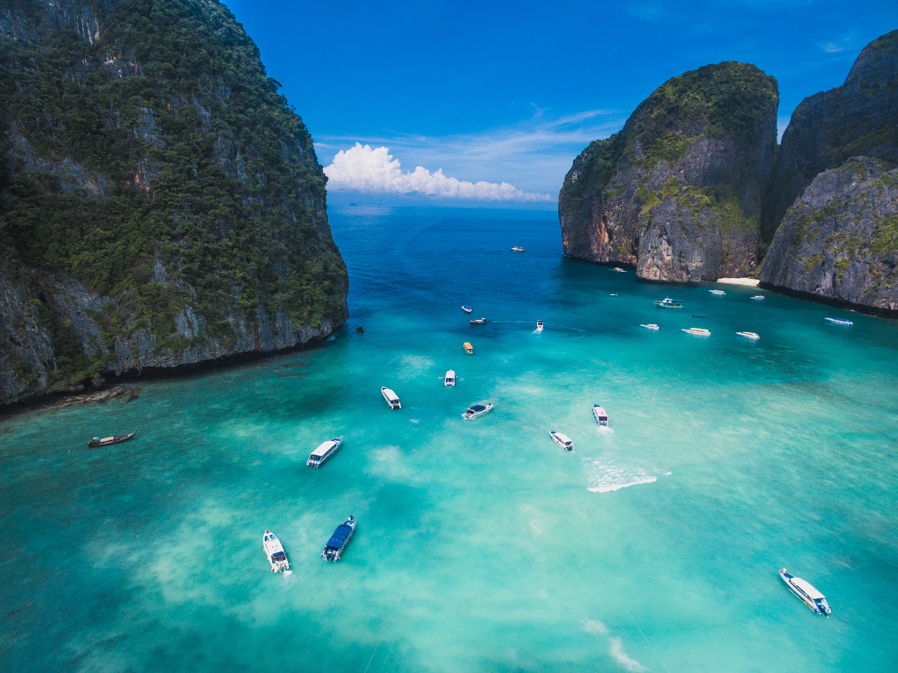 Boats on turquoise water below limestone cliffs of Maya Bay